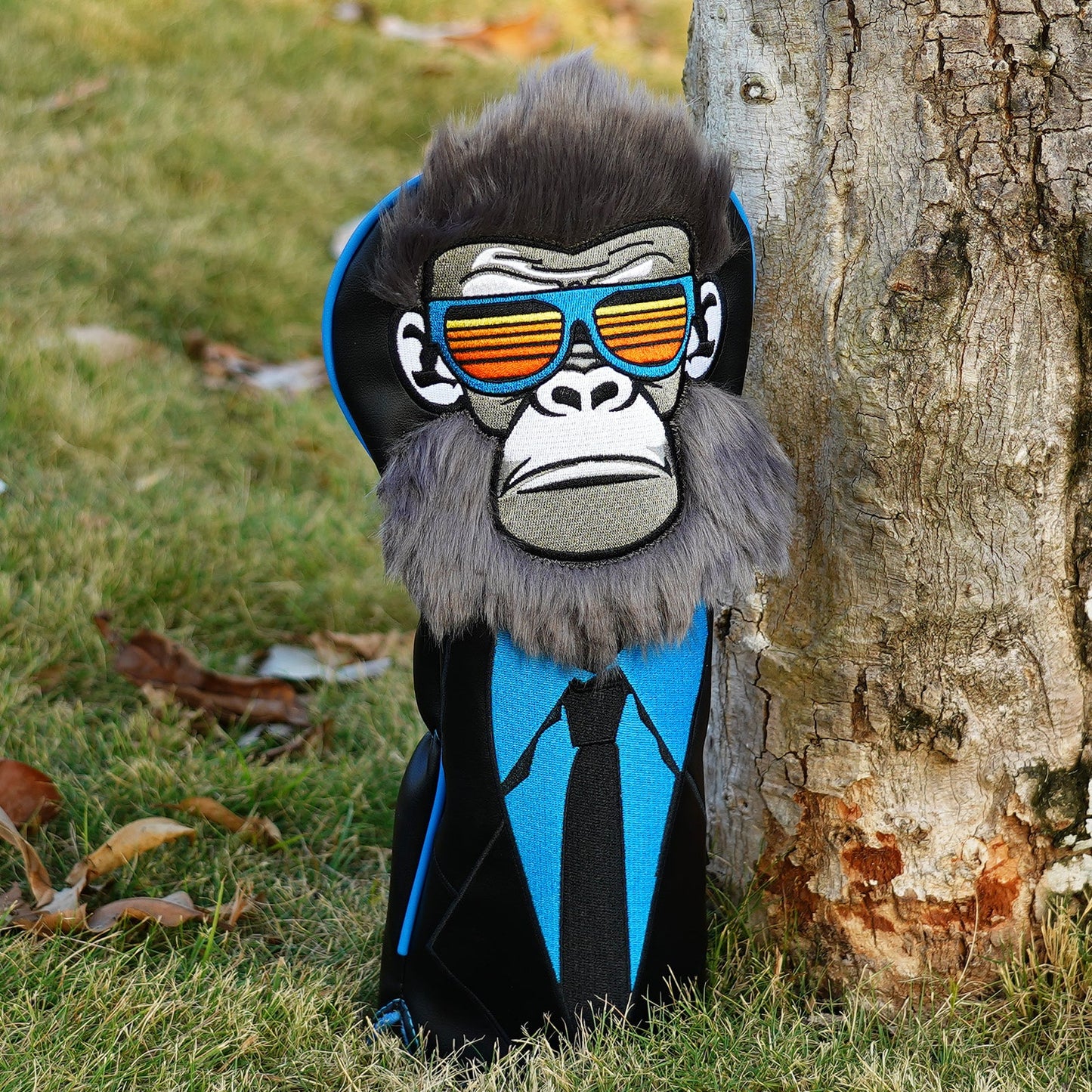 Gorilla-shaped golf head cover with sunglasses and tie leaning against a tree
